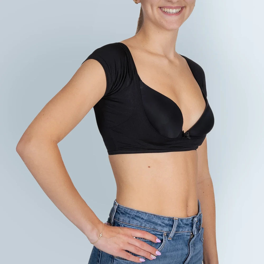 Vrouw model met zwarte ANTI ZWEET COLLEGE TOP van ConfidenceForAll en blauwe spijkerbroek schuin vooraanzicht in studio met lichtblauwe achtergrond