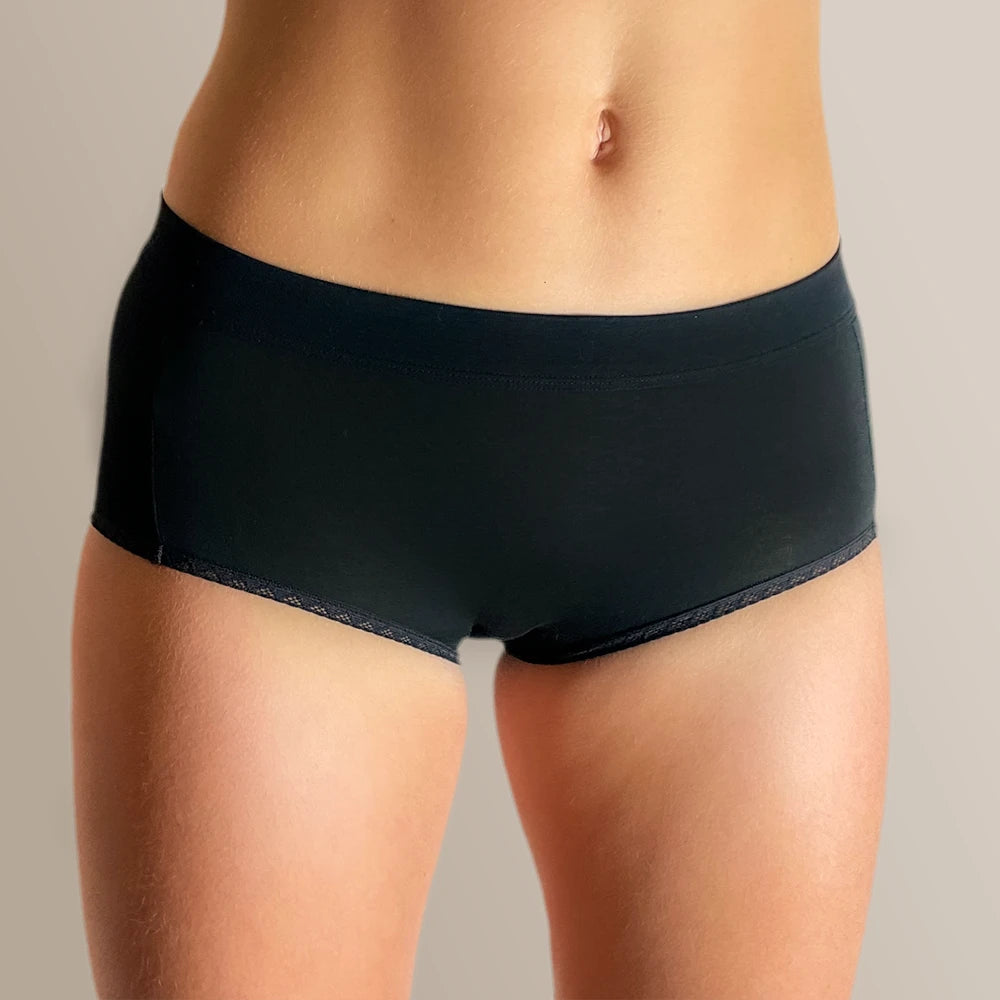 Studio foto van model in ConfidenceForAll anti-zweet damesondergoed in het zwart afgebeeld op zachte beige bruine achtergrond