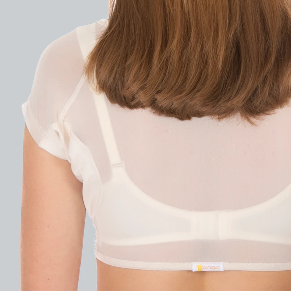 Studio foto van de achterkant van een vrouw die een ConfidenceForAll DryDress top draagt , een doorschijnend crème top met korte mouwen en zweetabsorberende, anti-transpirant zweetpads over een witte bh.