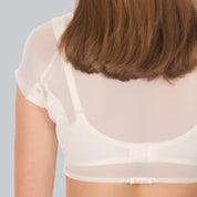 Studio foto van de achterkant van een vrouw die een ConfidenceForAll DryDress top draagt , een doorschijnend crème top met korte mouwen en zweetabsorberende, anti-transpirant zweetpads over een witte bh.