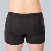 Studiofotografie van achterkant van een mannelijk model dat een zwarte, anti-transpirant boxershort met zweetpads van ConfidenceForAll draagt op een effen grijsblauwe achtergrond.