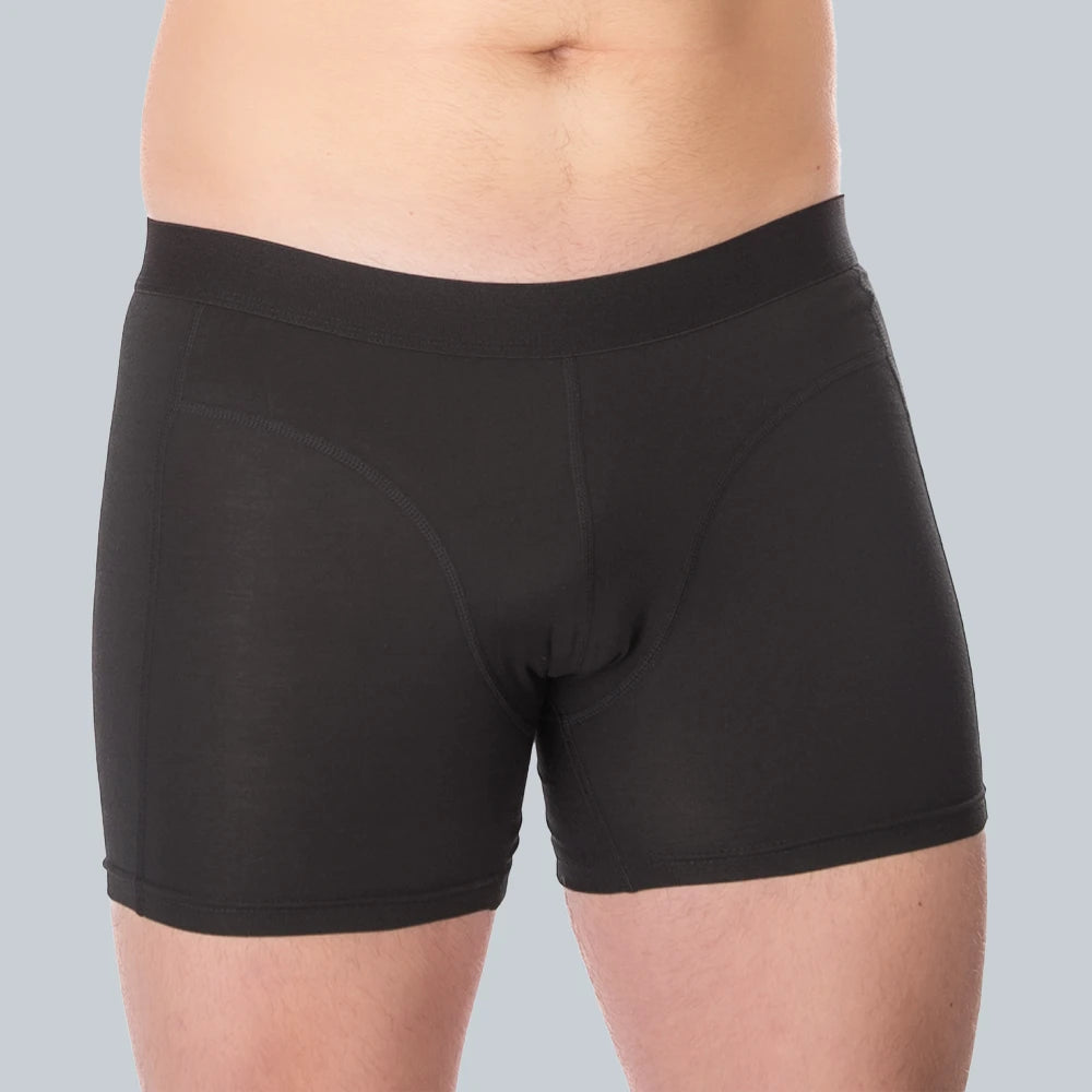 Studiofotografie van voorkant van een mannelijk model dat een zwarte, anti-transpirant boxershort met zweetpads van ConfidenceForAll draagt op een effen grijsblauwe achtergrond.