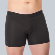 Studiofotografie van voorkant van een mannelijk model dat een zwarte, anti-transpirant boxershort met zweetpads van ConfidenceForAll draagt op een effen grijsblauwe achtergrond.