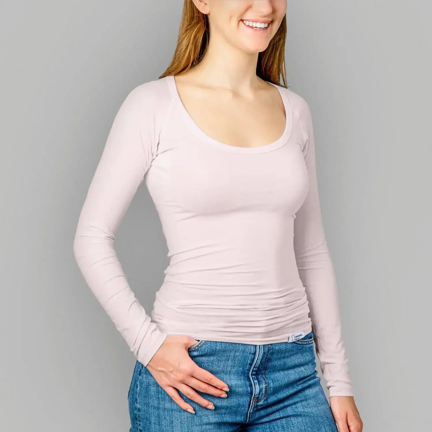 Front view studio photo of female model with blue jeans wearing anti-sweat shirt women undershirts with short sleeves from ConfidenceForAll in soft pink on a light gray background