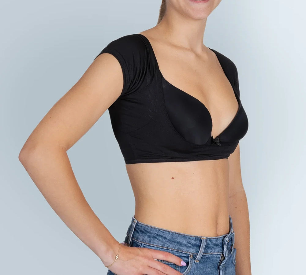 Vrouw model met zwarte ANTI ZWEET COLLEGE TOP van ConfidenceForAll en blauwe spijkerbroek schuin vooraanzicht in studio met lichtblauwe achtergrond