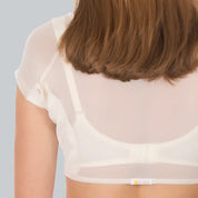 Studio foto van de achterkant van een vrouw die een ConfidenceForAll DryDress top draagt ​​, een doorschijnend crème top met korte mouwen en zweetabsorberende, anti-transpirant zweetpads over een witte bh.