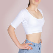 Een meisje draagt ​​een ConfidenceForAll Sweatproof witte crop top met korte mouwen en zweetpads die behandeld zijn met zilverionen en een lichtblauwe spijkerbroek. Ze staat met haar handen in haar zij tegen een lichtroze achtergrond.